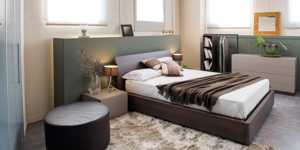 Modern luxury brown monochrome bedroom interior with large headboard above a double beds with cabinets, ottoman and built in wardrobe